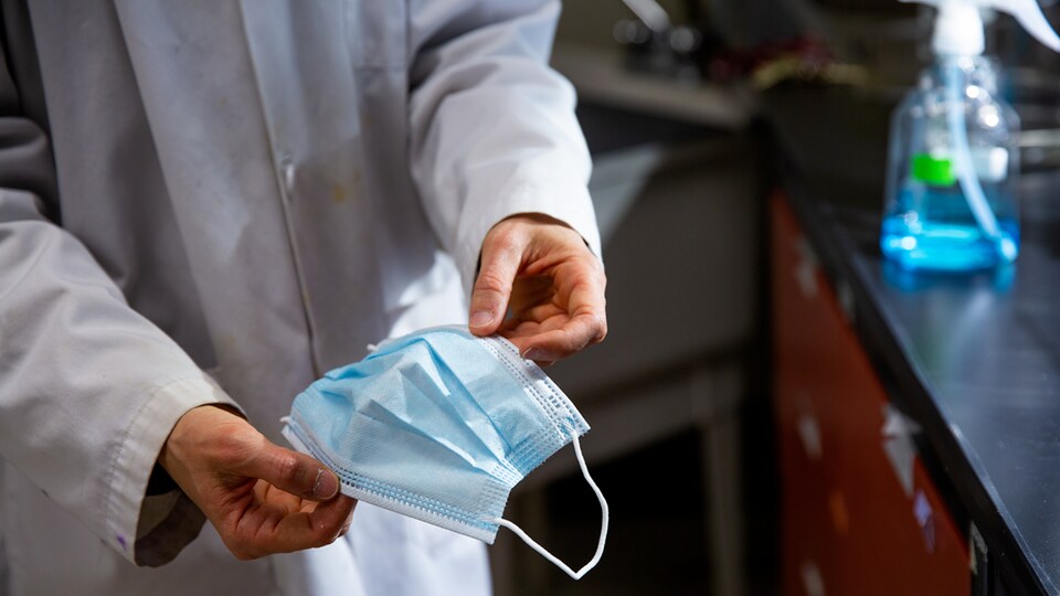 Un chercheur tient un masque chirurgical dans ses mains. 