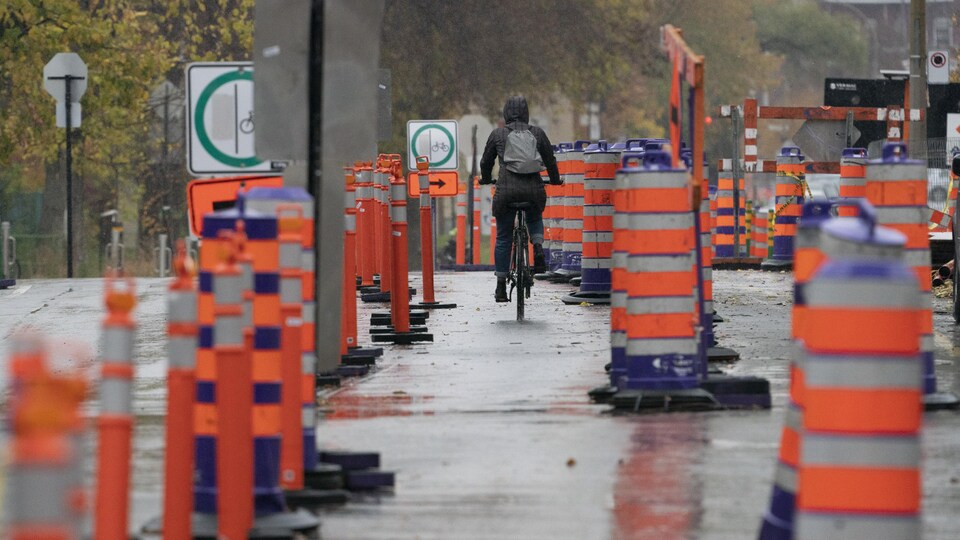 Un cycliste circule dans une rue où il y a des travaux et de nombreux cônes orange.