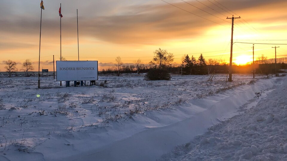 Le soleil se lève au loin sur une usine et une affiche sur laquelle on peut lire Fonderie Brunswick.