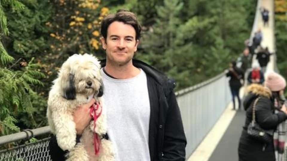 Un jeune homme tient un chien dans ses bras et se trouve sur un pont suspendu.