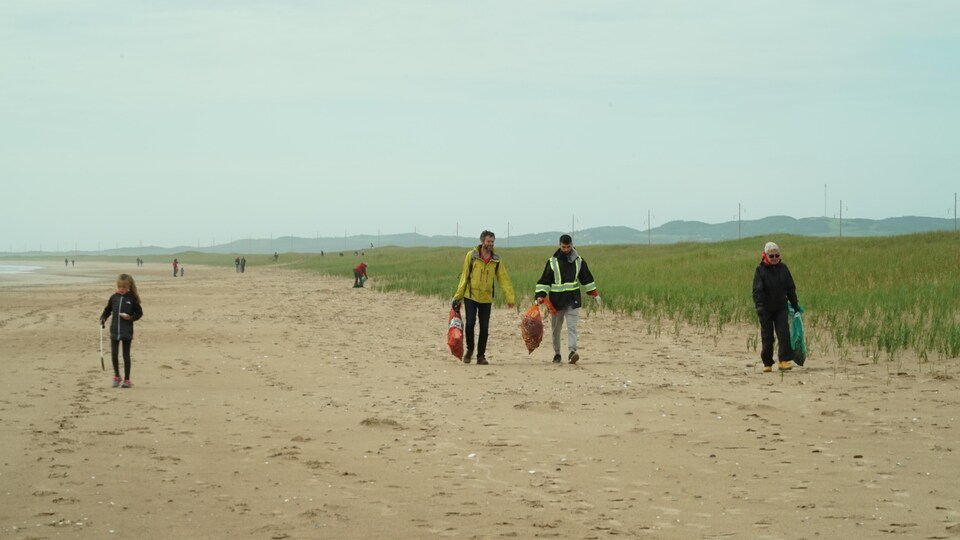Des gens marchent avec des sacs en mains sur une plage.