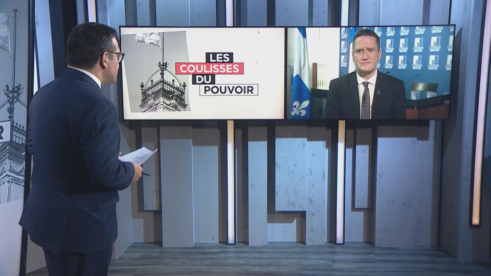 L'animateur Daniel Thibeault debout devant un écran où apparaît le ministre Charette.