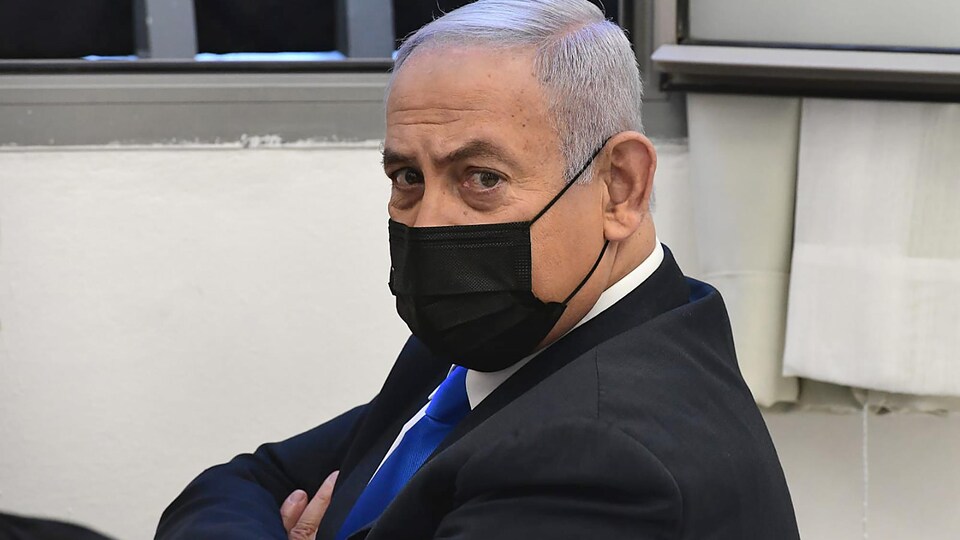 Benyamin Nétanyahou, assis dans une salle, le visage masqué, les bras croisés.