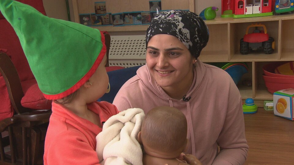 La dame qui regarde un enfant qui a un bébé jouet dans les mains.