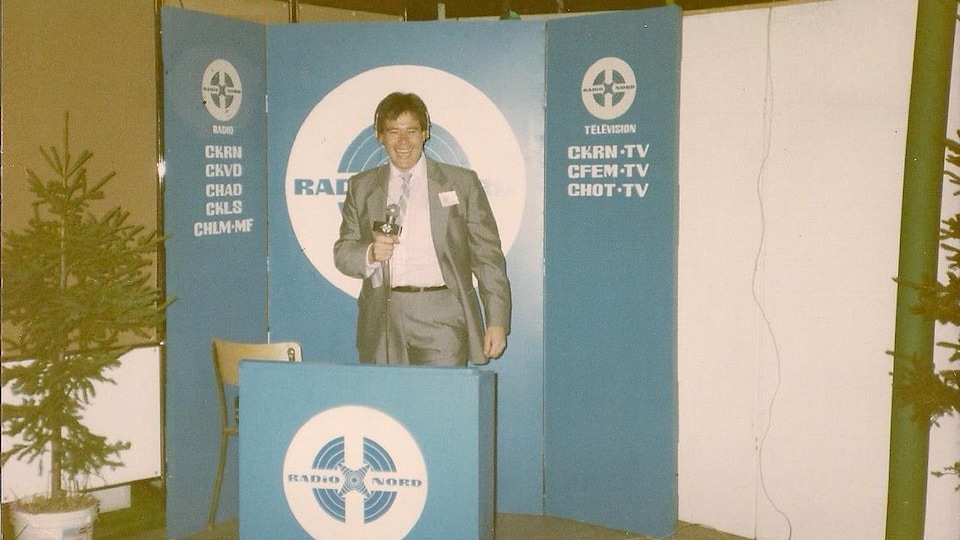 Un homme avec un micro derrière un lutrin de l'entreprise Radio Nord. 