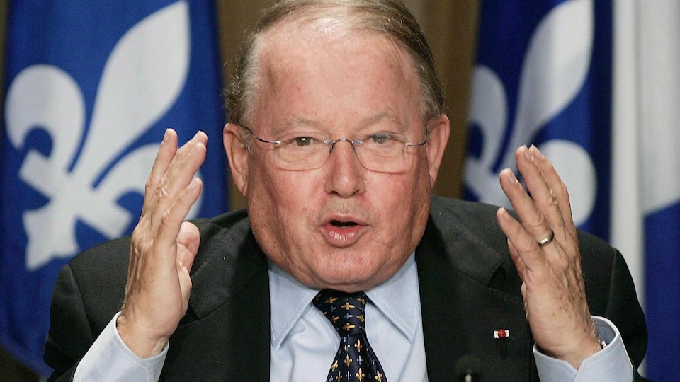 Bernard Landry brandit ses mains devant un micro avec le fleurdelisé derrière lui.
