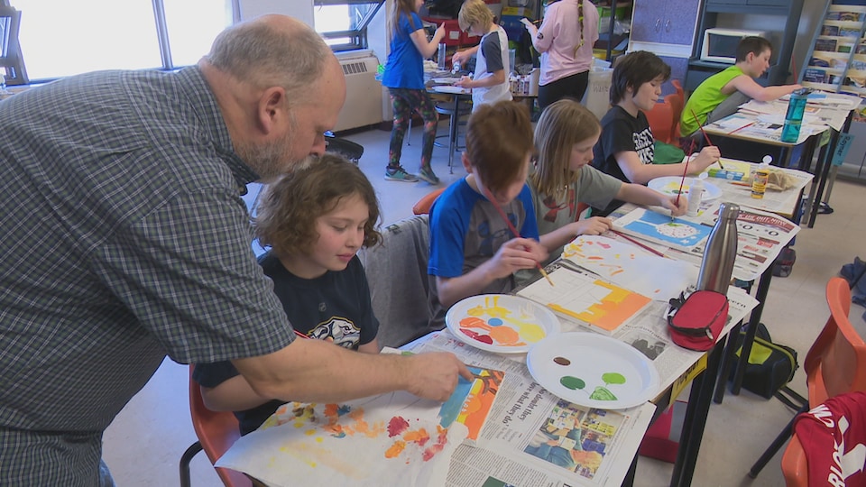 L'artiste Maurice Bernard en classe aide une élève à peindre un petit tableau