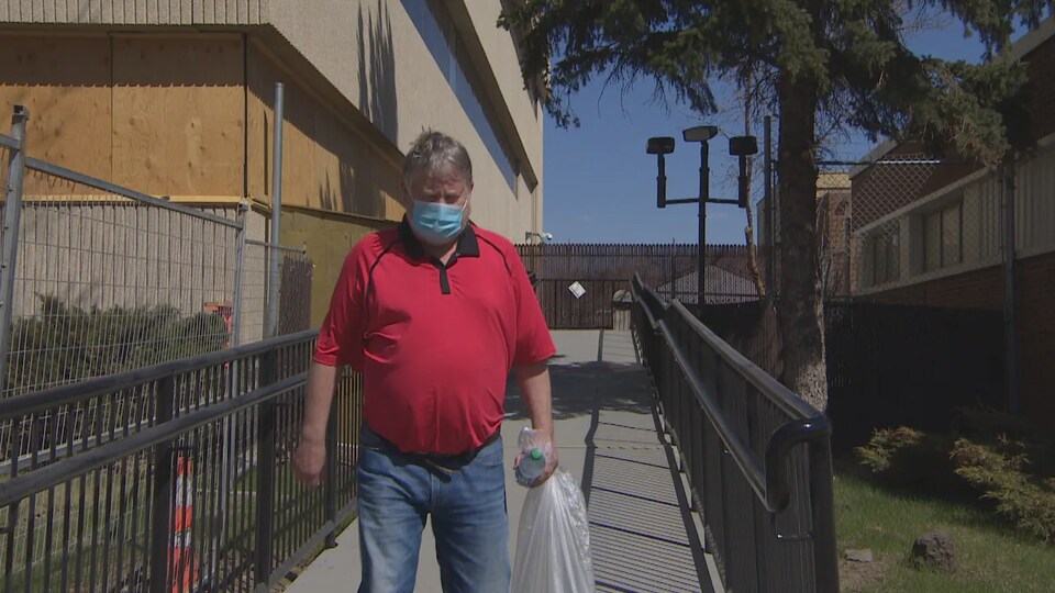 Un homme tient un sac et une bouteille dans la main et porte un masque.