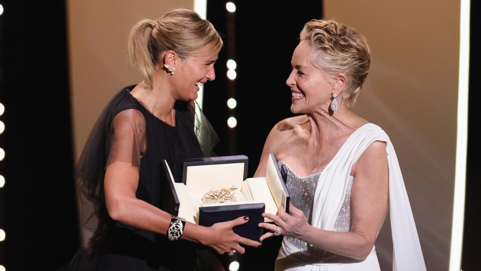 Deux femmes sourient sur scène en tenant la Palme d'or. 