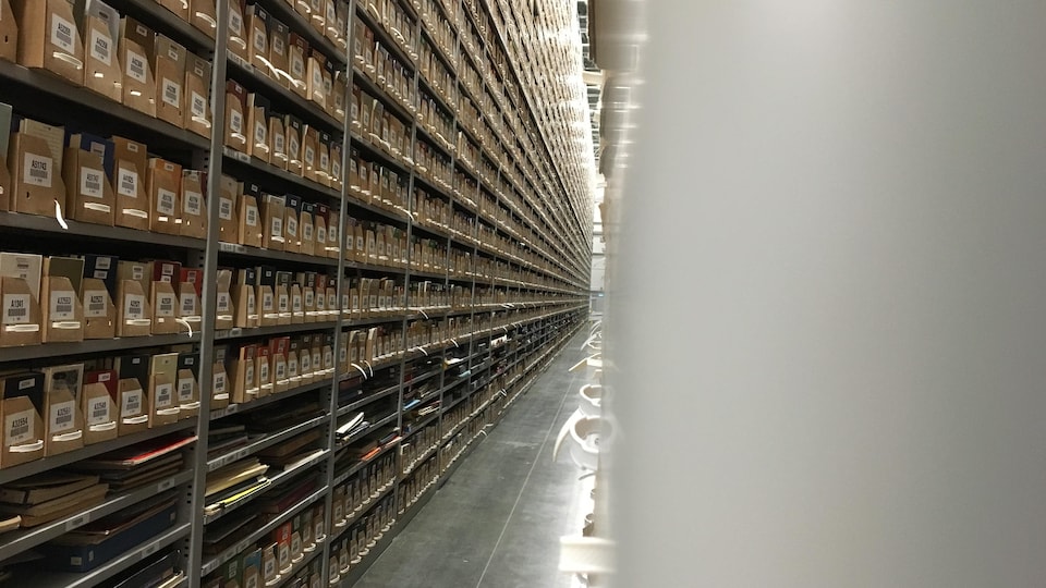 Une allée du centre d'archives avec des boîtes posées sur chaque étagère.