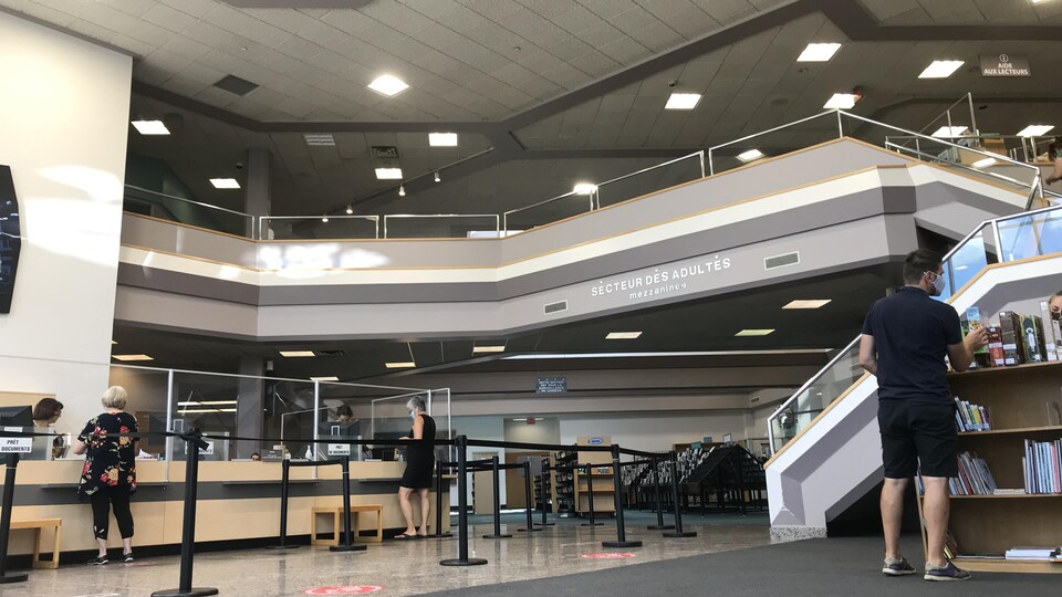 Quelques usagers, portant le masque, à l'intérieur de la bibliothèque.