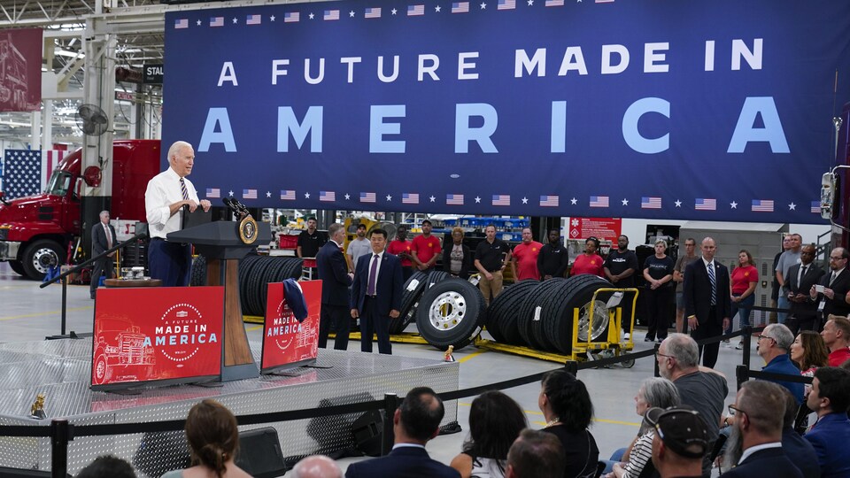 Devant une immense bannière disant « Un avenir fait en Amérique » disposée au-dessus de pneus, le président Joe Biden, sans son veston, s'adresse à des travailleurs d'une usine de l'entreprise Mack Trucks, en Pennsylvanie.