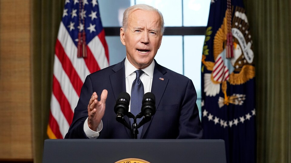 Joe Biden parle dans un micro, derrière un lutrin arborant le logo du président des États-Unis et devant le drapeau américain.