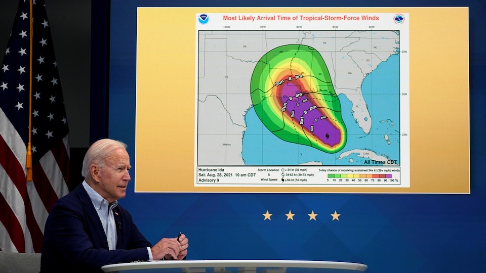 Joe Biden assis à une table, un graphique d'un ouragan affiché derrière lui.