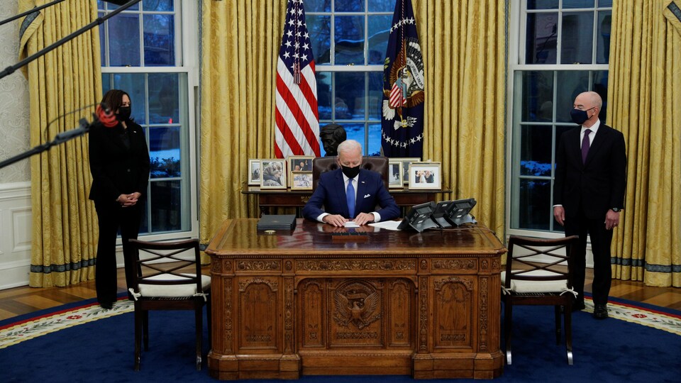 Joe Biden, à son bureau dans le bureau ovale, signe un décret sous le regard de Kamala Harris et Alejandro Mayorkas.