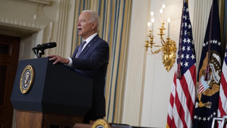 On voit le président de profil, qui prononce une allocution dans une pièce de la Maison-Blanche. Derrière lui, des drapeaux américains.
