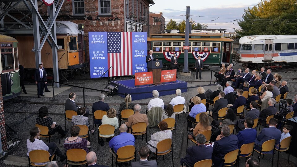 Joe Biden, vu de loin, s'adresse à un auditoire réuni dans le musée, où se trouvent des trolleys; sur la scène sont disposées des affiches avec le slogan « Reconstruire en mieux ».