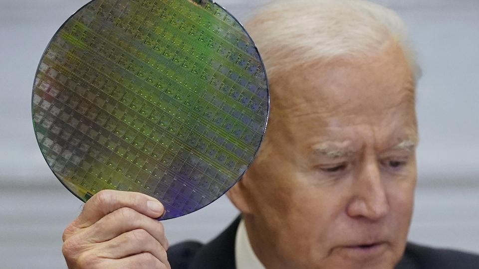 Le président Biden brandit une plaque de matériau semi-conducteur, que l'on voit en gros plan.