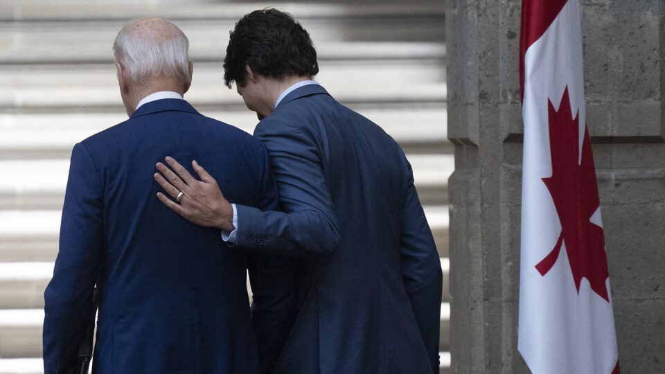 Joe Biden et Justin Trudeau de dos, à côté d'un drapeau du Canada.