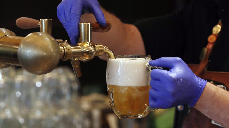 Un serveur ganté verse de la bière en fut dans une pinte.