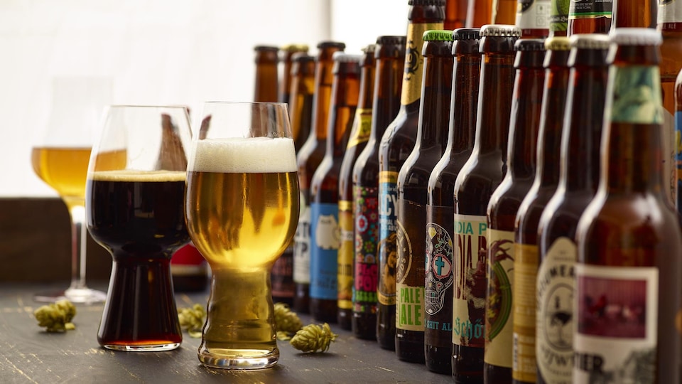 Plusieurs bouteilles de bières différentes et trois verres de bière remplis sont disposés sur une table.