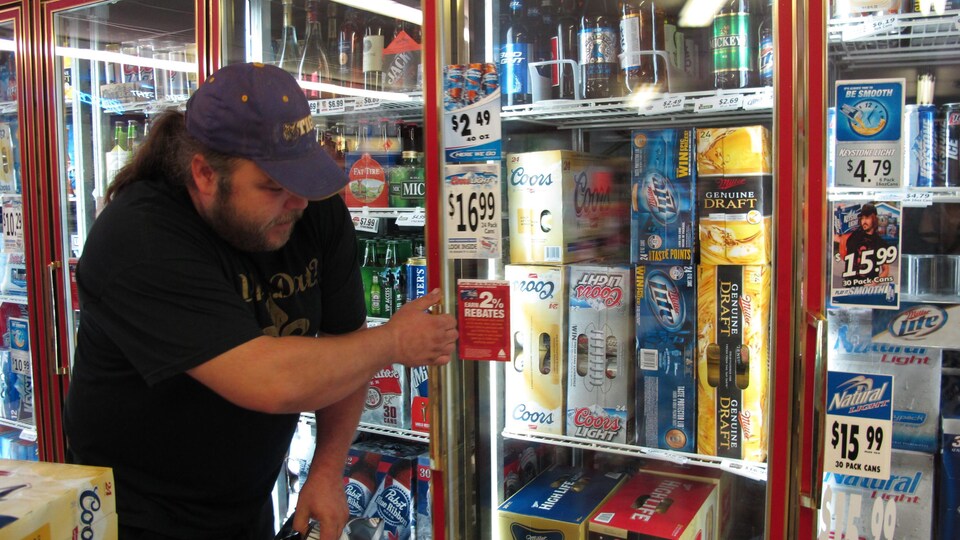 Un homme prend une caisse de bière dans le réfrigérateur d'un dépanneur.