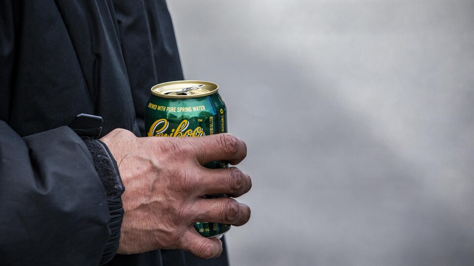 La main d'un homme tient une cannette de bière.