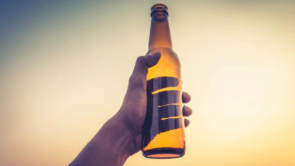 Une main tenant une bouteille de bière vide.