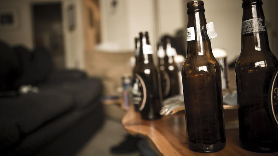 Des bouteilles de bière vides sur déposées sur une table dans le salon d'un appartement.