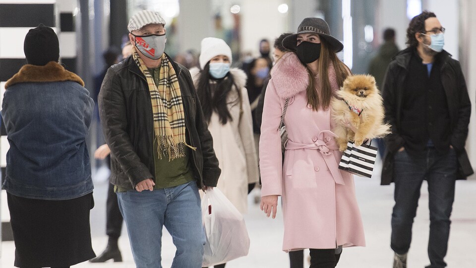 Les gens portent des masques, une passante tient son chien dans sa main.