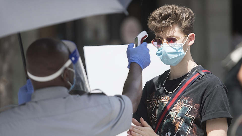 Un jeune homme portant un masque se fait prendre sa température par un agent de sécurité.