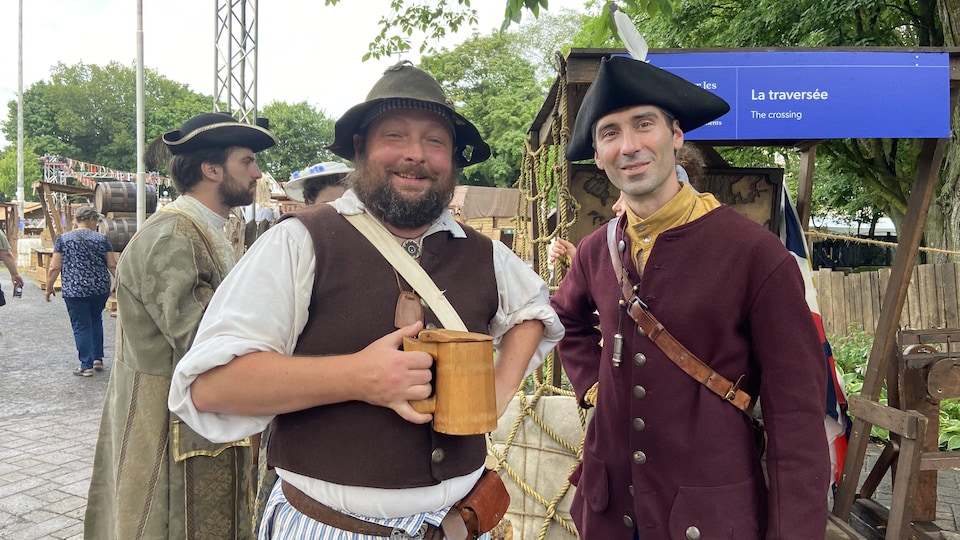 Deux hommes en costumes du 18e siècle, l'un en paysan qui tient une chope de bière à la main et l'autre en soldat avec un tricorne sur la tête.
