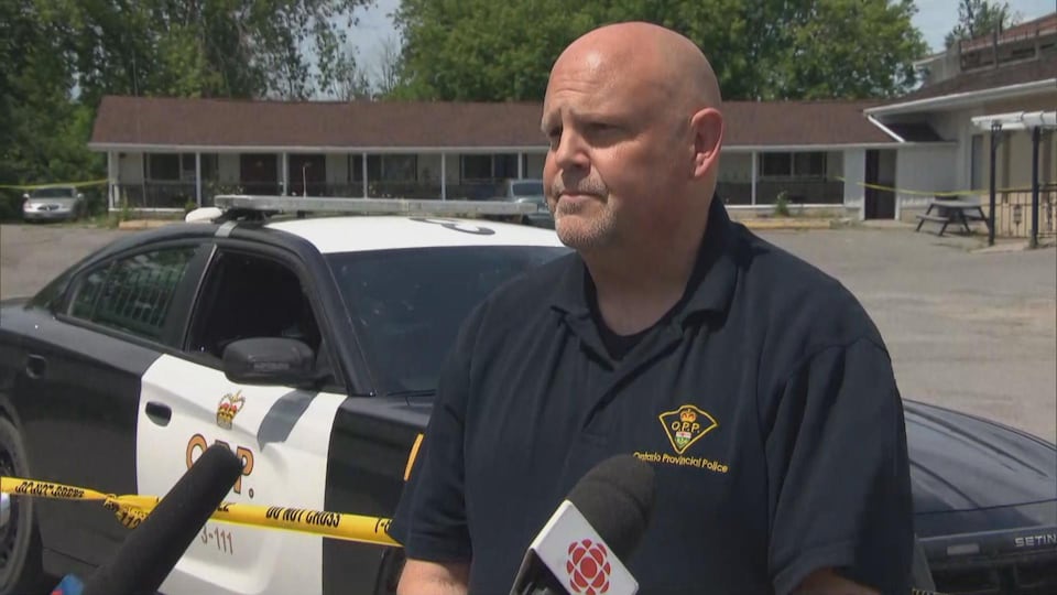 Un porte-parole de la Police provinciale de l'Ontario devant une scène de crime et une voiture de la PPO parle aux médias.