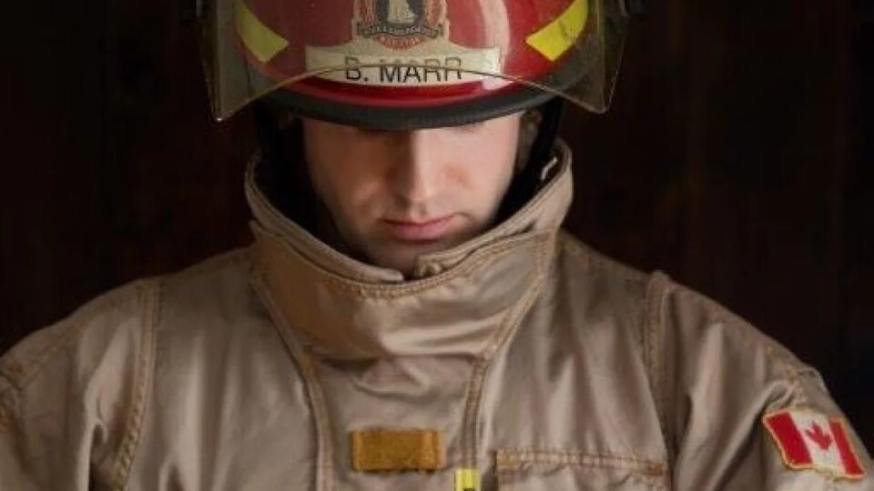 Bill Marr vêtu de son uniforme de pompier tient le nouveau-né qui porte un ensemble crocheté rouge et jaune.