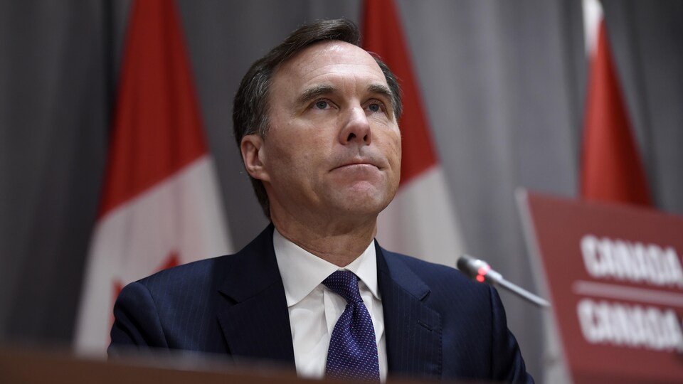 Bill Morneau assis derrière une tribune de la presse.