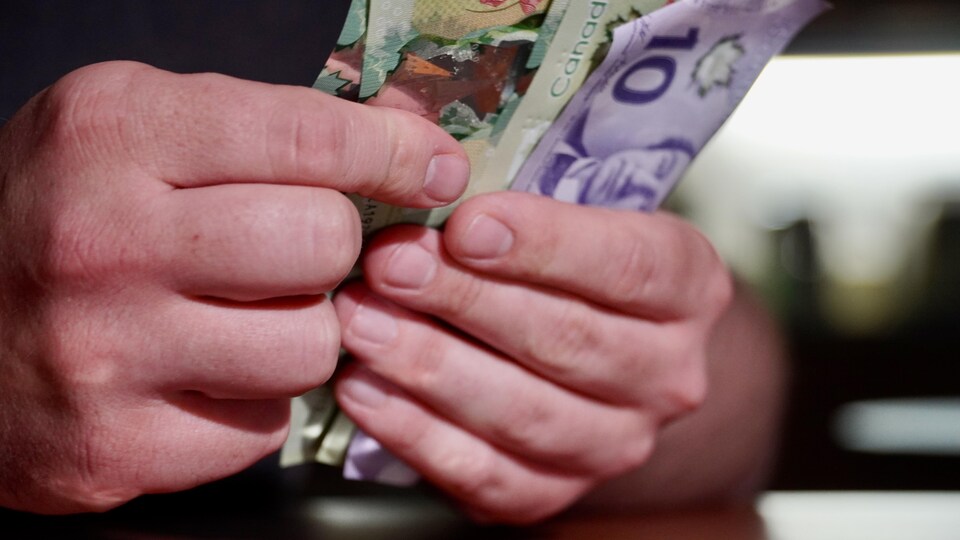 Des billets d'argent dans une main et de la monnaie sur la table.