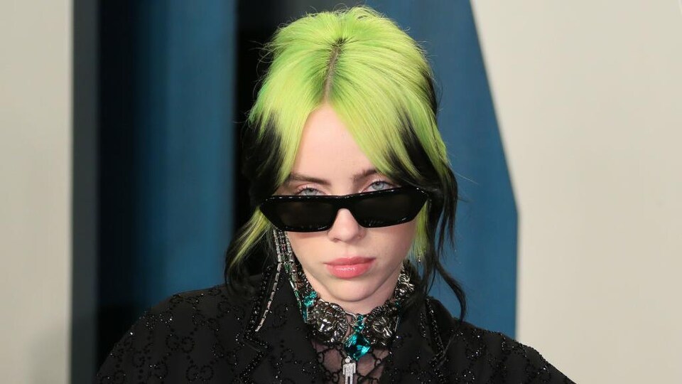 Billie Eilish, les cheveux verts, porte des lunettes de soleil. 