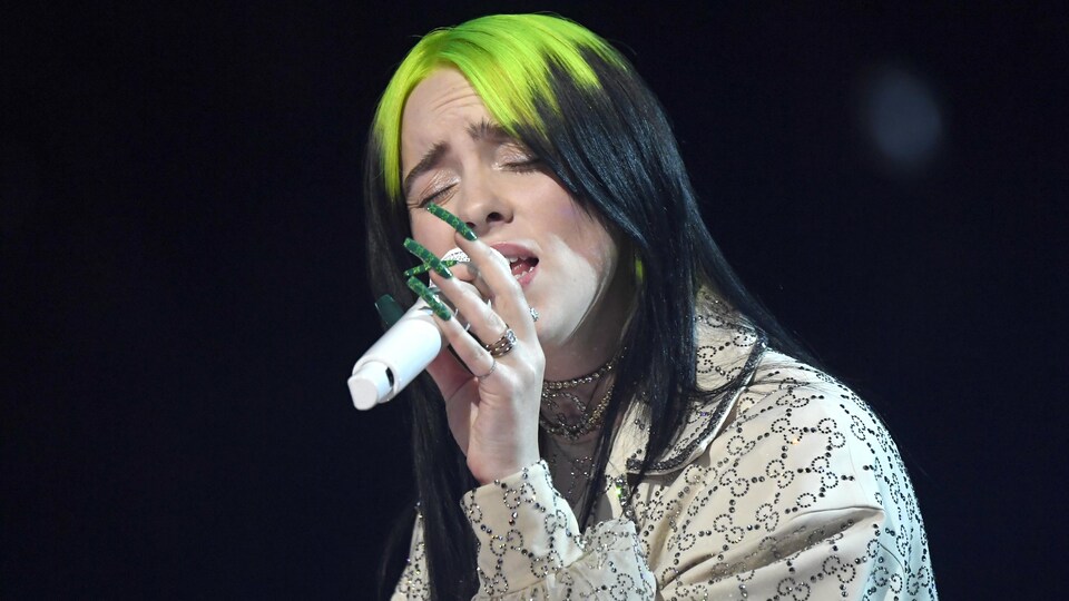 Billie Eilish chante, un micro à la main.