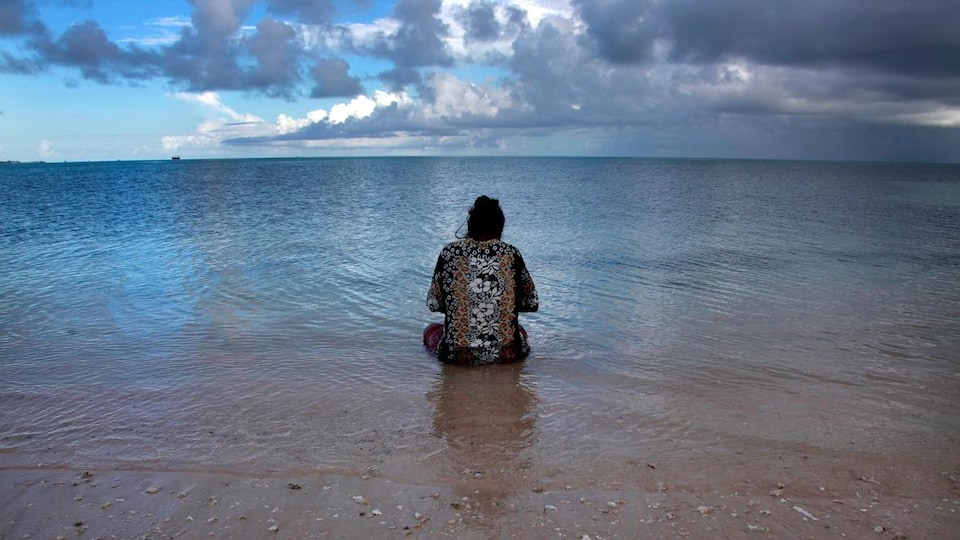 Une femme est assise dans l'eau face à l'océan.