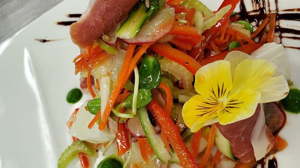 Des légumes et une fleur comestible rassemblés dans une assiette.