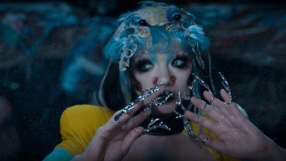 L'artiste islandaise avec des ongles qui ressemblent à des coraux, des cheveux bleus et un chandail jaune.