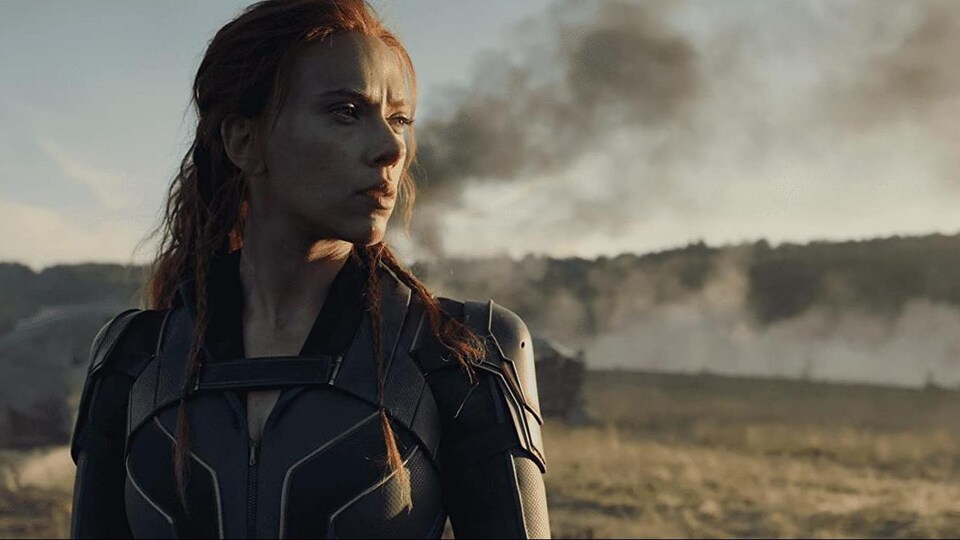 Une femme vêtue d'un costume de superhéroïne observe l'horizon. Un panache de fumée noire est visible à l'arrière-plan.
