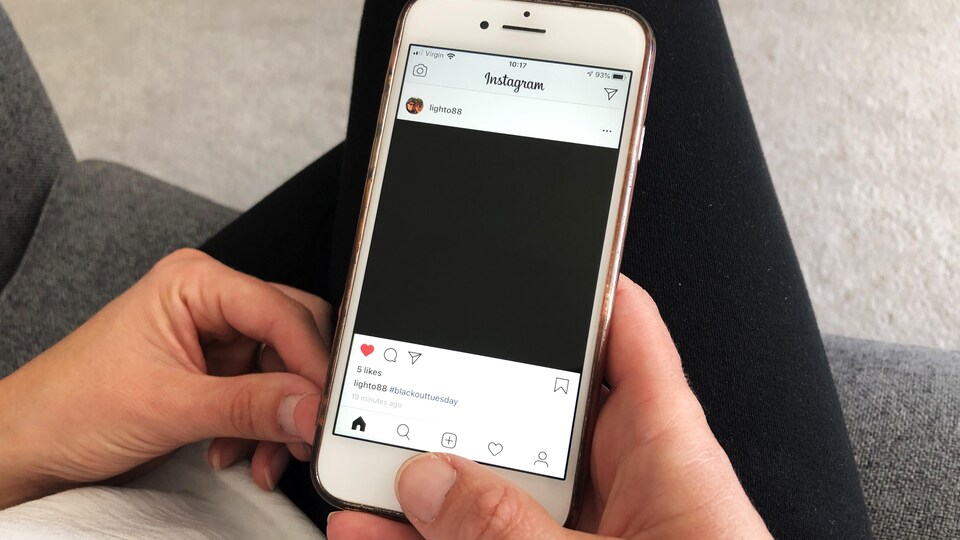Un homme tient un téléphone intelligent dans la main. L'application Instagram est affichée et l'on voit la publication d'une photo entièrement noire.