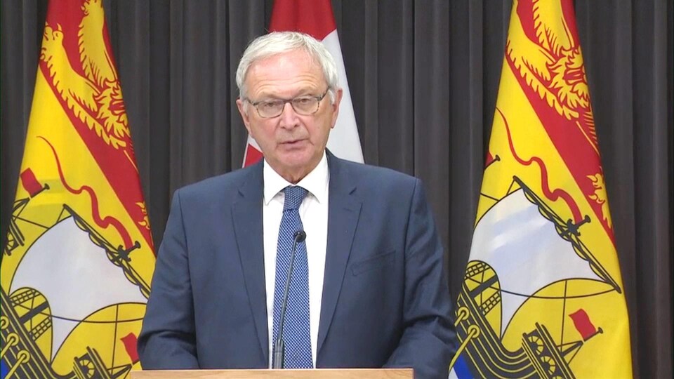 Blaine Higgs en conférence de presse devant des drapeaux du Nouveau-Brunswick.