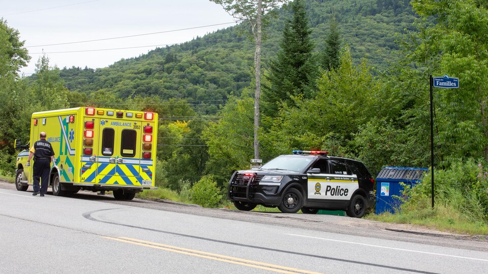 Une voiture de police et une ambulance garées sur une route bordée d'arbres et de végétation.