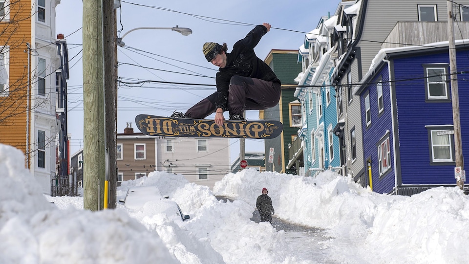 Un homme saute en planche à neige dans une rue après une tempête de neige.