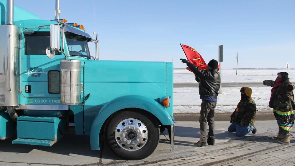 Un camion arrêté devant trois manifestants.