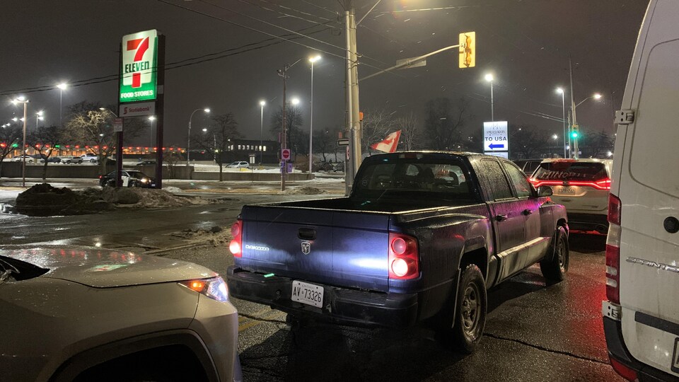 Des véhicules immobilisés sur la route; un drapeau canadien en arrière-plan.