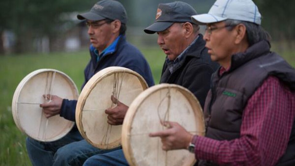 Trois hommes assis jouent du tambour.
