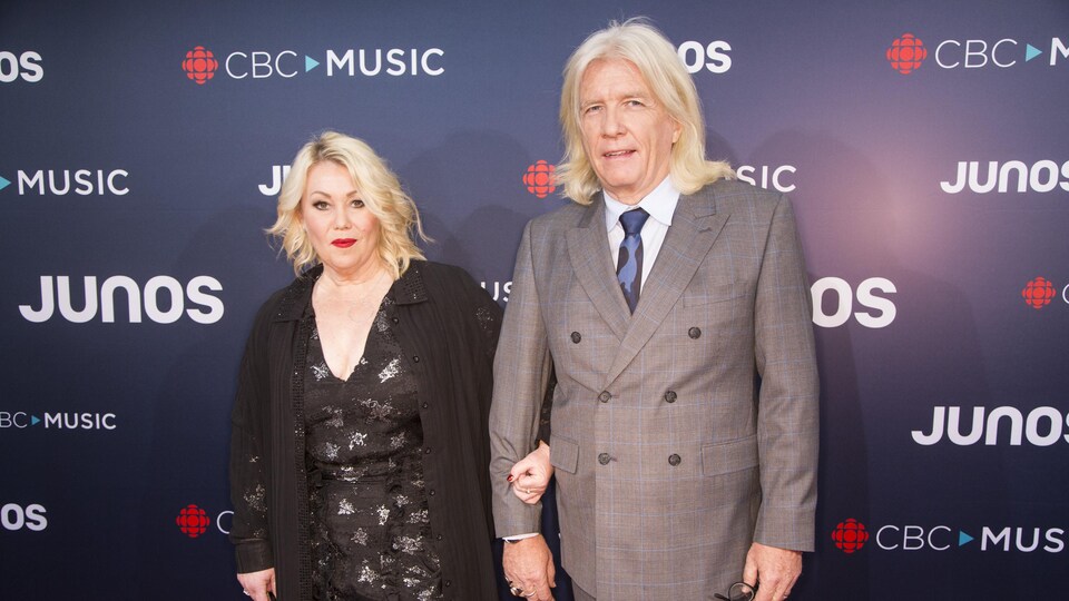 Une femme et un homme prennent la pose devant un mur avec les logos de CBC et des prix Juno.